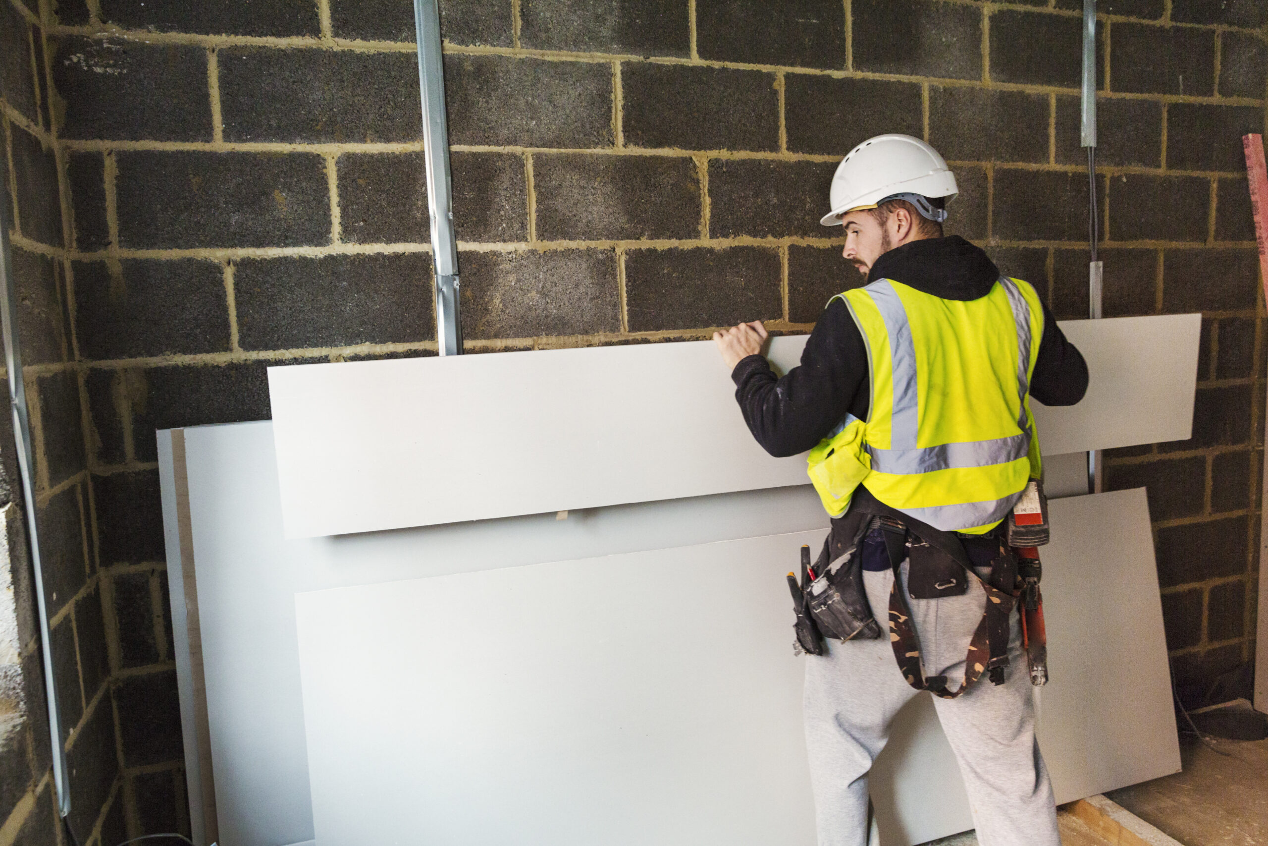 A workman in hard hat and high vis jacket stacking wood against a wall at a construction site. ,Construction Site,England