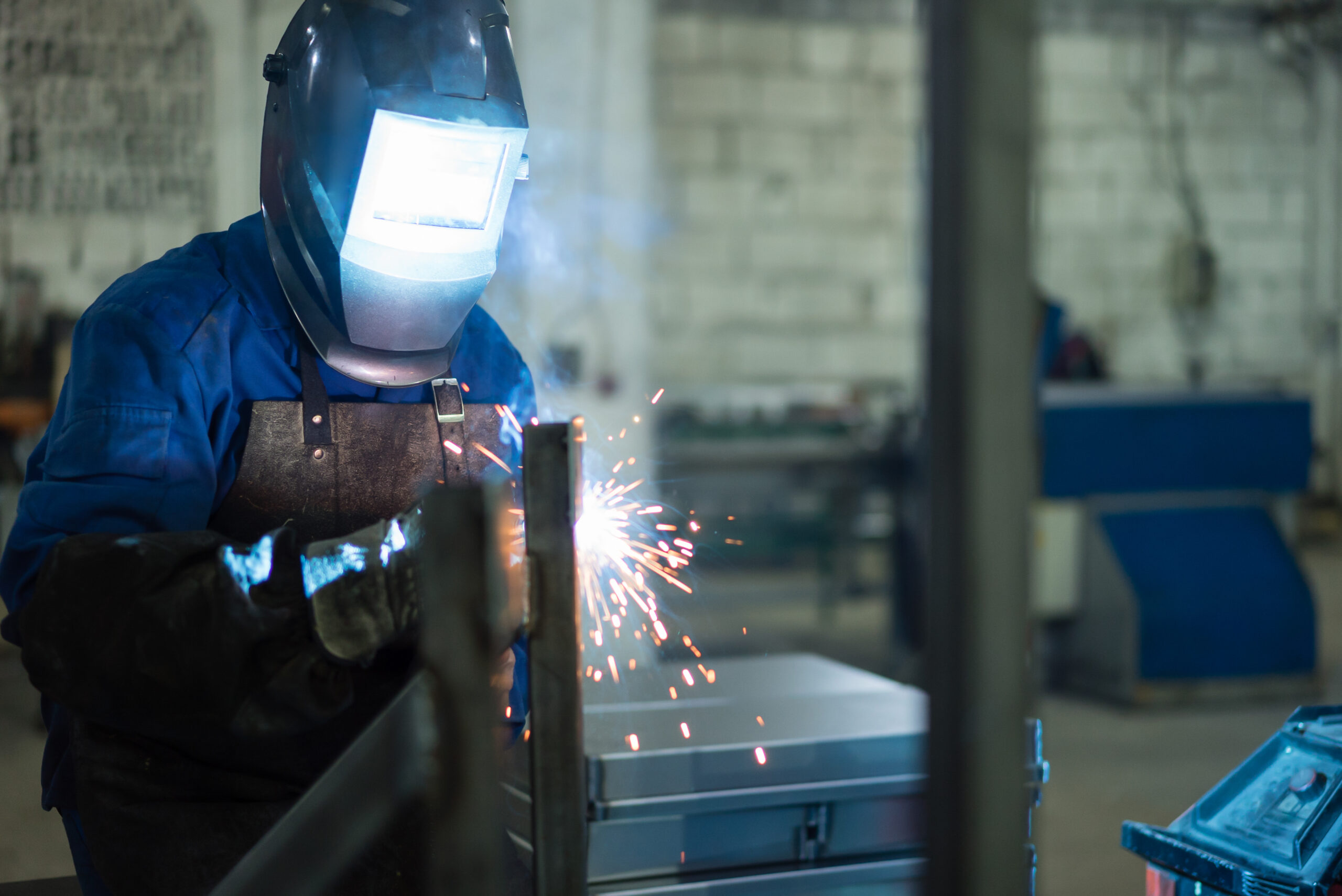 worker in protective gear, welding square pipes
